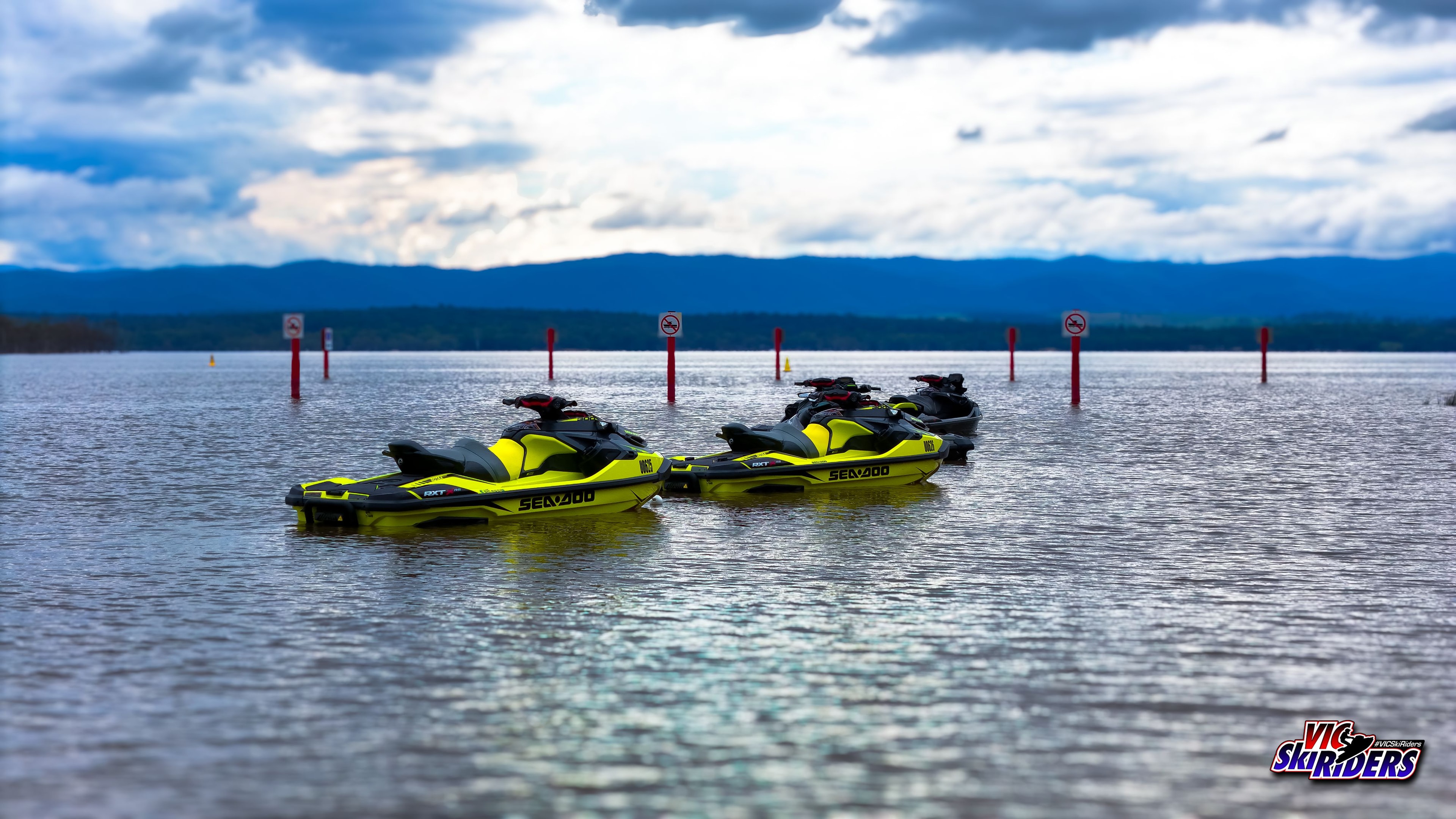 Five yellow Sea-Doo RXT jet skis floating on a calm lake with mountain backdrop
